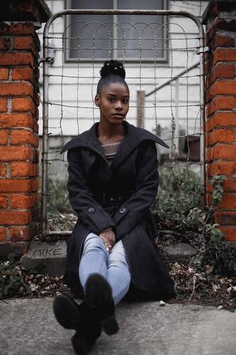 Young black woman sitting in front of a gate staring into the camera. This represents that sometimes we feel as if we need to protect ourselves. Sacred Circle Holistic Healing offers therapy for codependency for adults in Kansas.