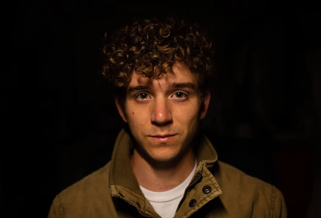Photo of young man in a jacket in front of a black background representing someone who has attending counseling for Highly Sensitive People and is feeling excited about life after having realized that being an HSP is a good thing. Maggie Jones Boyle offers therapy for Highly Sensitive People online throughout the state of Kansas.