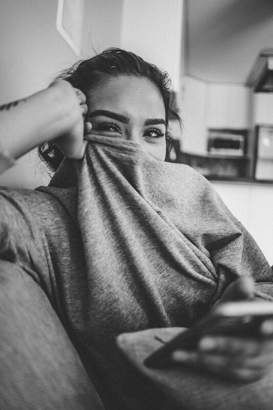 Black and white picture of young woman smiling, her mouth hidden behind her shirt. This illustrates that HSPs experience conflict differently than non-HSPs. Maggie Jones Boyle offers therapy for HSPs in Lawrence, Kansas.