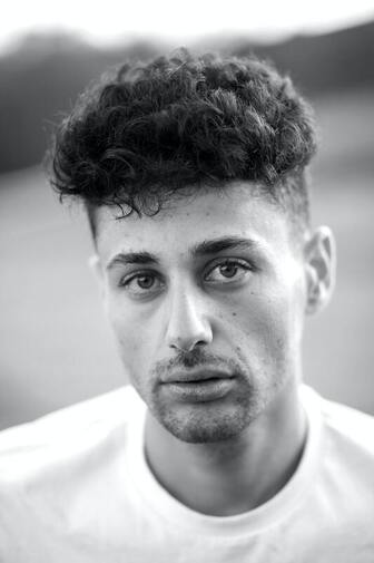 Black and white photo of a young man looking into the camera with a subtle sadness. This illustrates what grief feels like in the body. Sacred Circle Holistic Healing offers online grief counseling in Kansas for adults.