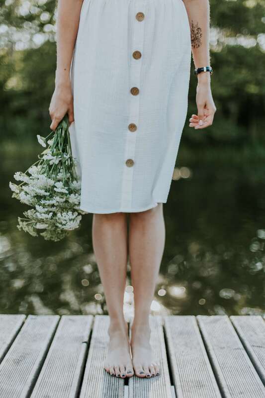 Young woman with tattoo holding white yarrow. This illustrates that I work with young adults who are struggling with anxiety, low self-esteem, and boundary issues.