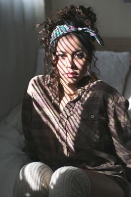 Young woman with curly hair sitting by a window with light filtering across her face. This illustrates that Sacred Circle Holistic Healing offers therapy for young adults in Lawrence, Kansas.
