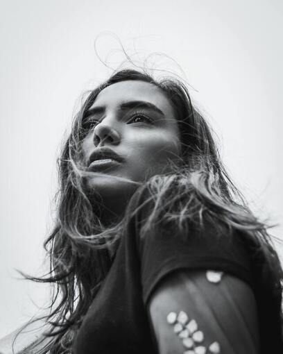 Black and white portrait of a young white woman with long, straight hair looking over camera. This illustrates that Sacred Circle Holistic Healing offers therapy for young adults struggling with anxiety and low self-worth in Lawrence, Kansas.