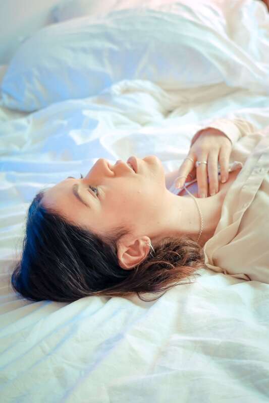 Young woman lying on a bed, staring up on the ceiling. This represents someone feeling sad before they come to therapy with Sacred Circle Holistic Healing in Lawrence, Kansas, 66044.