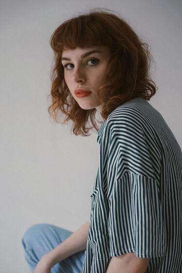 Young woman looking into the camera, wearing a pinstriped shirt. This represents that Sacred Circle Holistic Healing offers online counseling services in Kansas for self-esteem, anxiety, and codependency.
