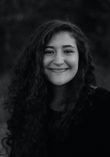 Black and white photo of a young woman with long, dark hair smiling into the camera. This illustrates the benefits to mental health when we practice self-acceptance.