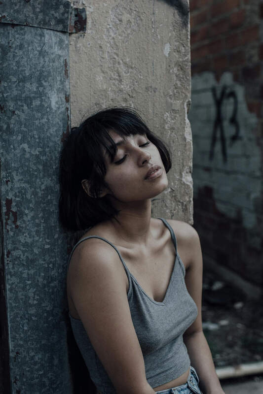 A picture in a gray tanktop leaning against a wall. Represents the pain of childhood trauma and complex PTSD.