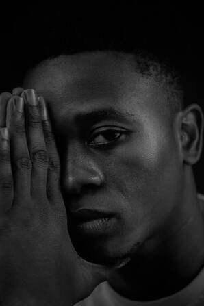 Close up black and white portrait of a Black man, looking into the camera with his hands up supporting his face. This illustrates the pain for grief and that Sacred Circle Holistic Healing offers grief counseling in Lawrence, Kansas.