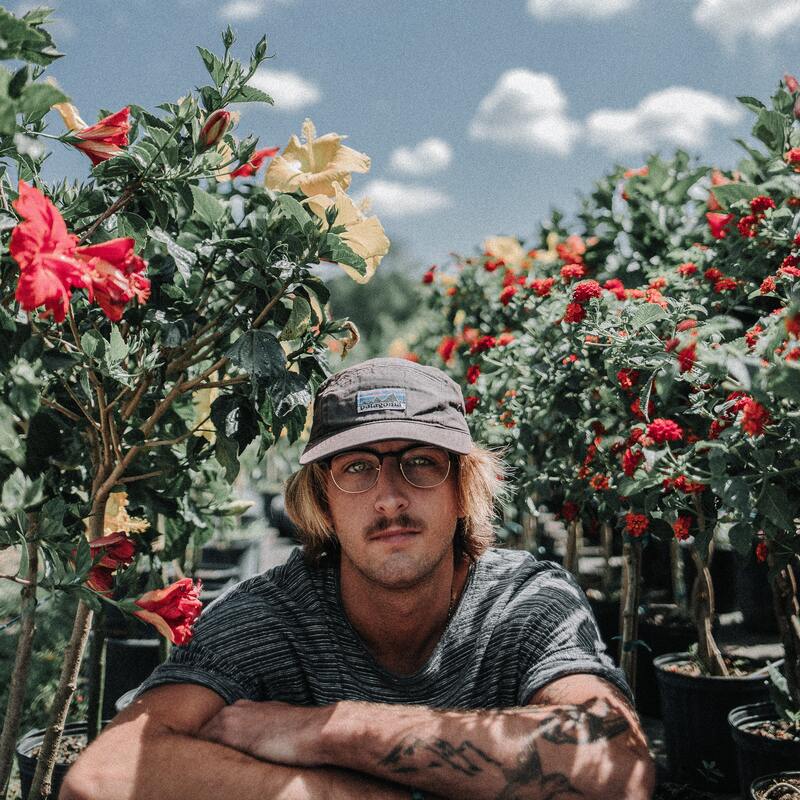 Man sitting in front of hibiscus in the daytime. This illustrates that all adults have an inner child. Maggie Jones Boyle offers online inner child therapy in Lawrence, Kansas.