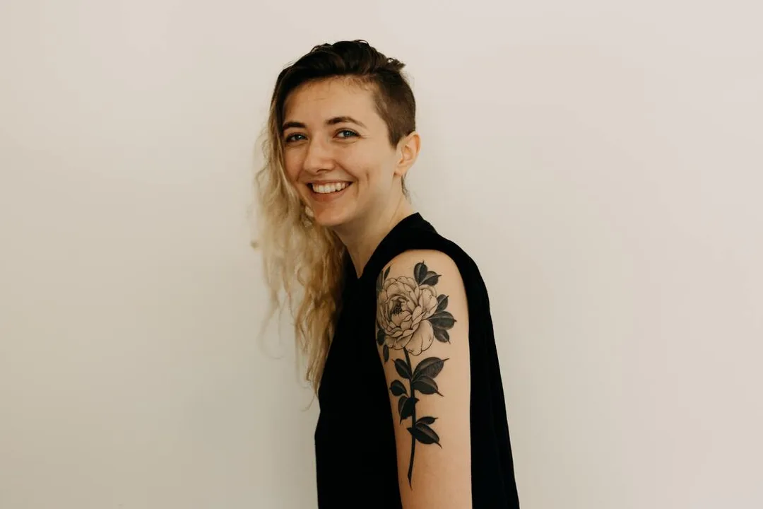 White woman with tattoo smiling at the camera. This represents that Sacred Circle Holistic Healing offers online counseling in Kansas for young adults who have low self-esteem and anxiety.