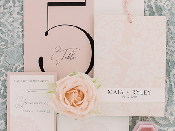 Layered invitation with floral pink pattern on top, attached with pink tassel, reply card with pink flower and pink border, large table number on pink paper
