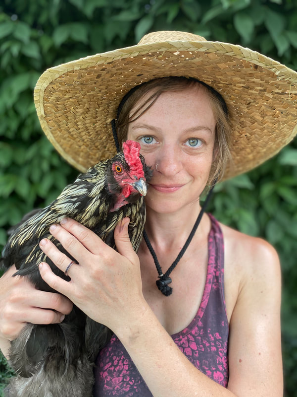 Thirty-something white woman wearing a straw hat holds a black and gold rooster.
