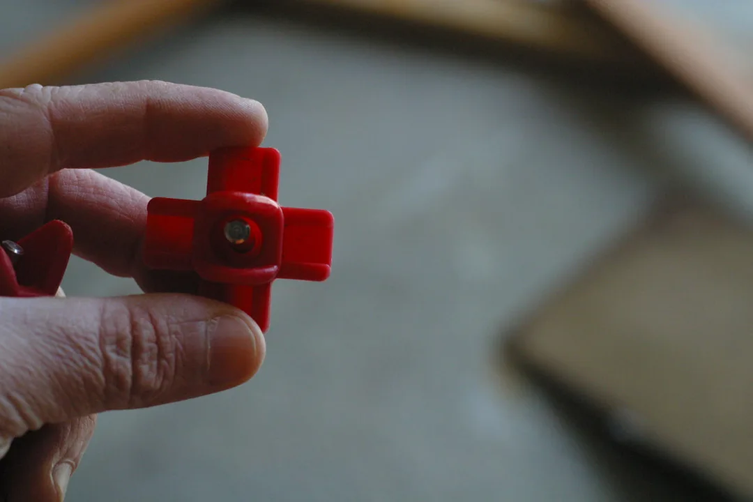 White hand holding a red plastic water nipple