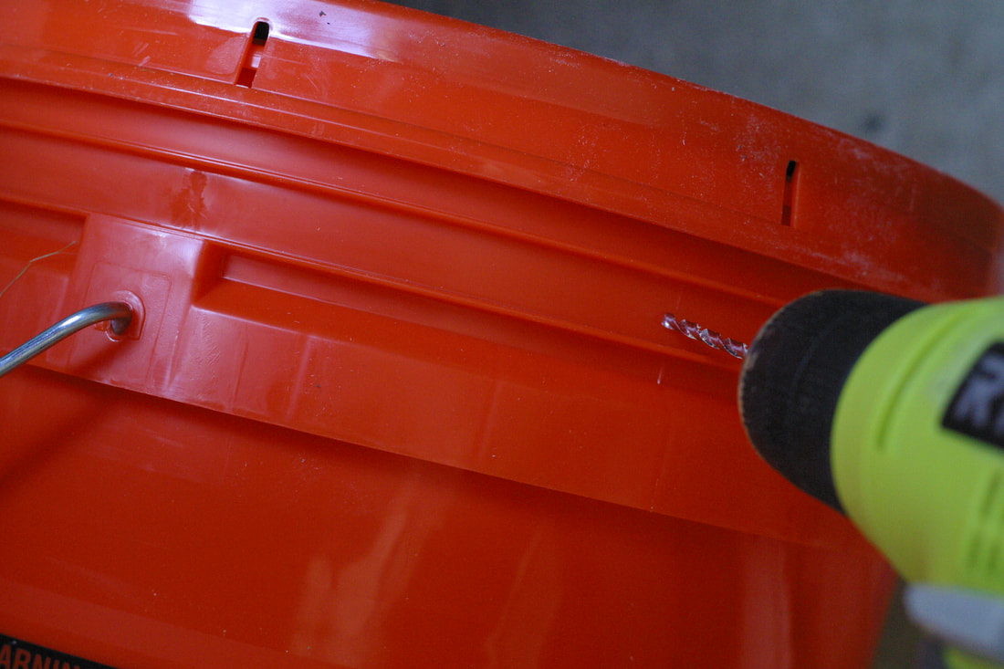 Drilling holes in an orange 5 gallon bucket to make a DIY chicken waterer.