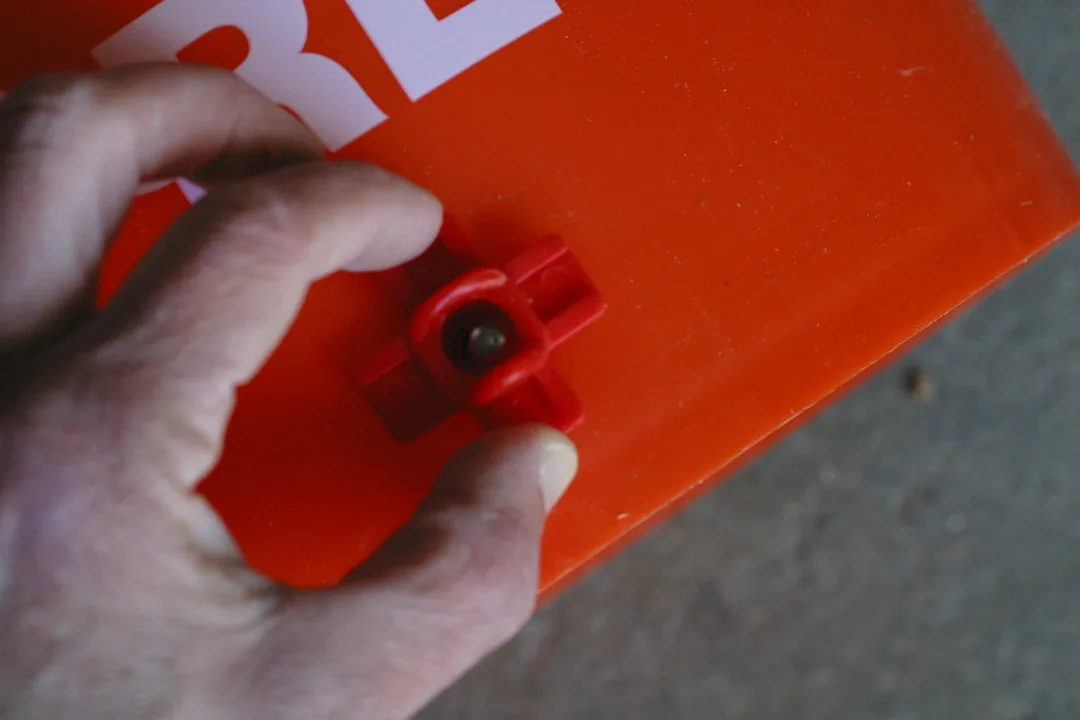 White hand attaching a side mount nipple to a five gallon bucket while making a DIY chicken waterer.