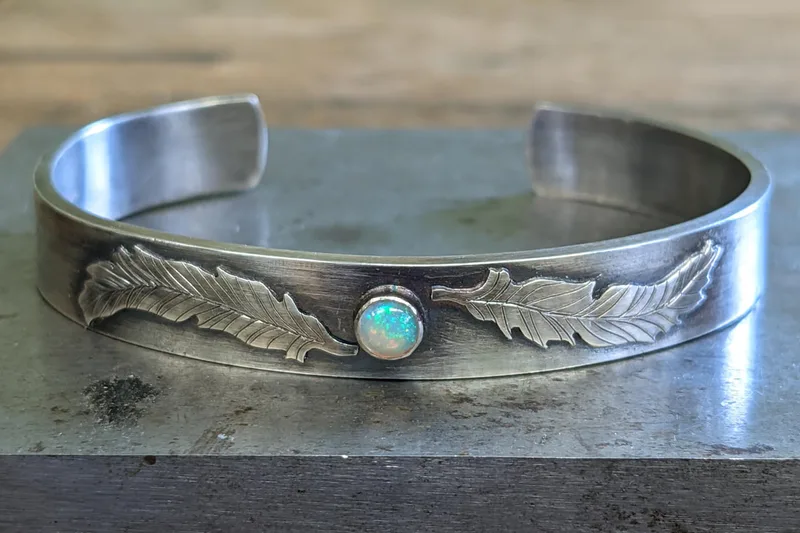 silver cuff with decorative feather details and opal