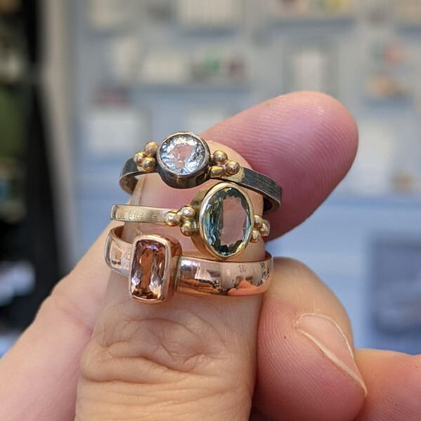 A hand holding 3 rings with bezel set stones