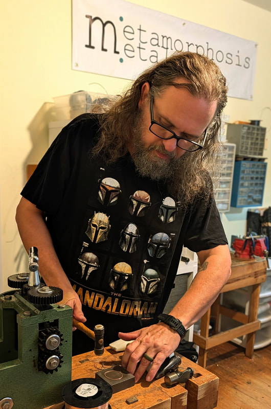 A man standing at a workbench hammering a circle of metal