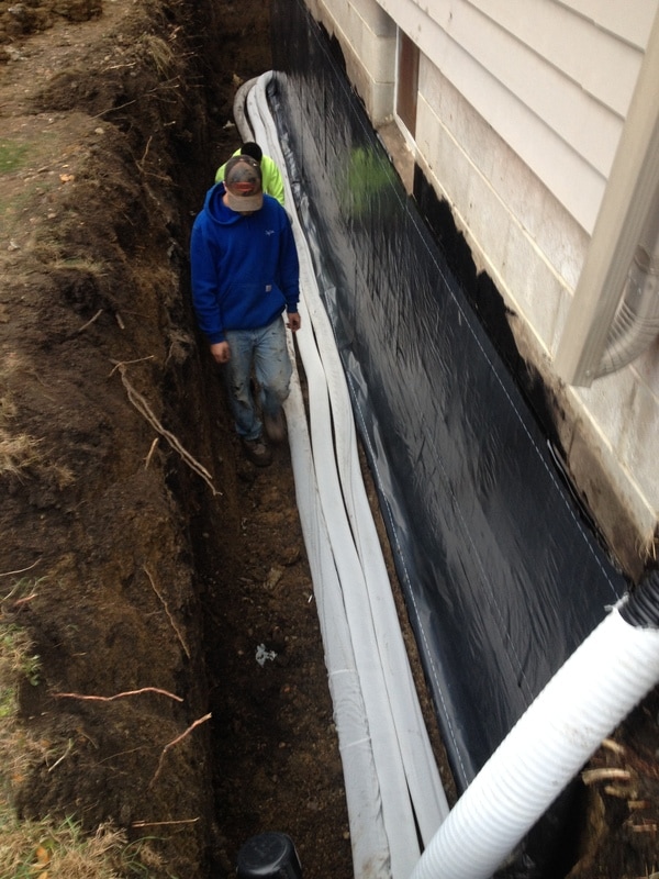 Installing rubber membrane to block walls and drain tile for waterproofing.