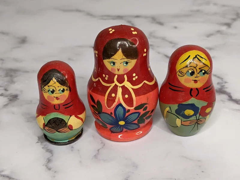 A set of three painted wooden Russian nesting dolls that are magnets with red, green, and pink painted clothing.