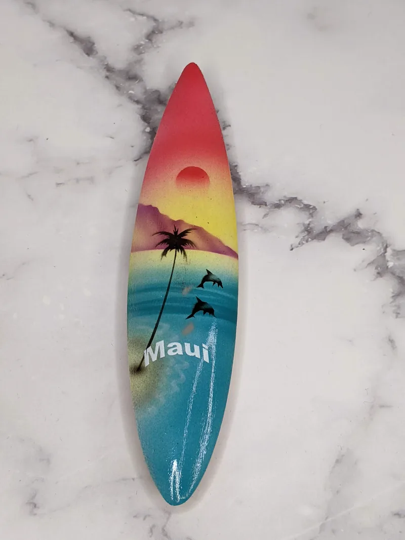 A vintage wooden surfboard-shaped magnet with a painted Maui design.