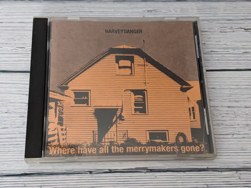 A CD by Harvey Danger, "Where have all the merrymakers gone?" in a plastic case with an image of a yellowish-orange house on the cover.