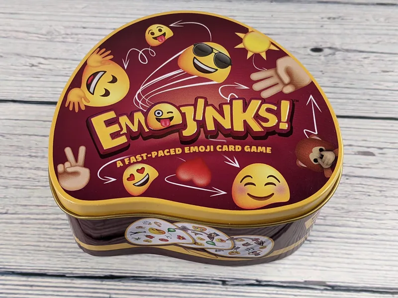 A burgundy-colored tin with yellow emoji images, that includes a card game called Emojinks!