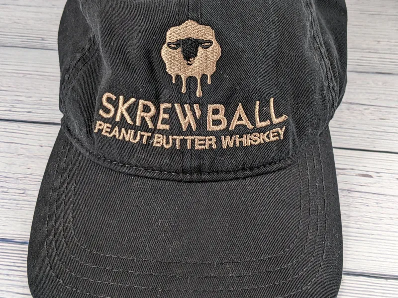 A black cap with a tan embroidered image of a sheep and the Skrewball brand.