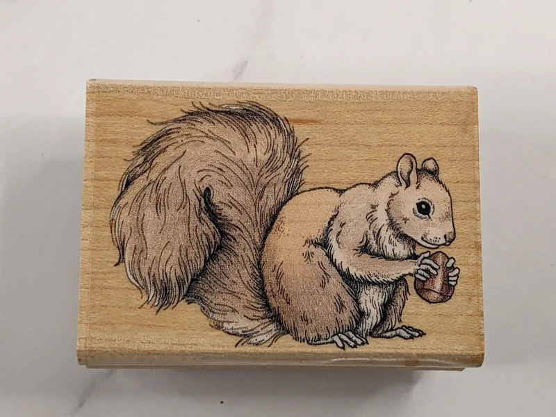 A wood-mounted rubber stamp with an image of a squirrel holding and eating a nut.