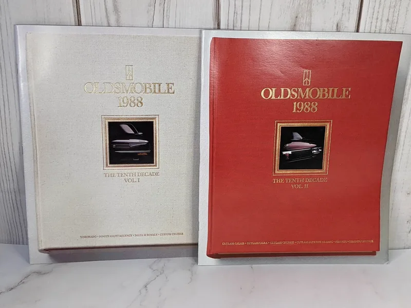 A pair of books that are sales brochures for 1988 Oldsmobiles. One book has a white cover and the other one is red.