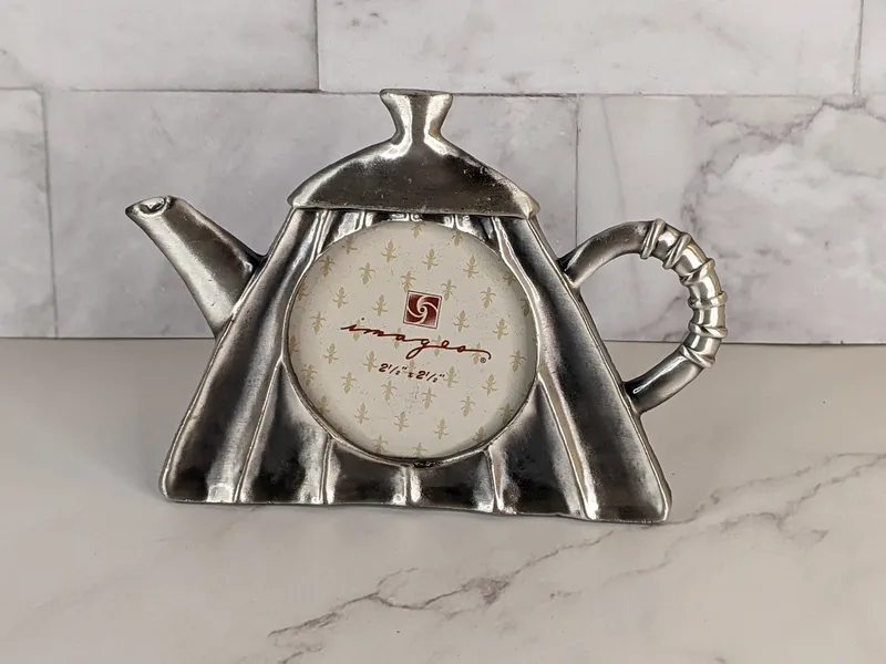 A silver metal photo frame shaped like a teapot.