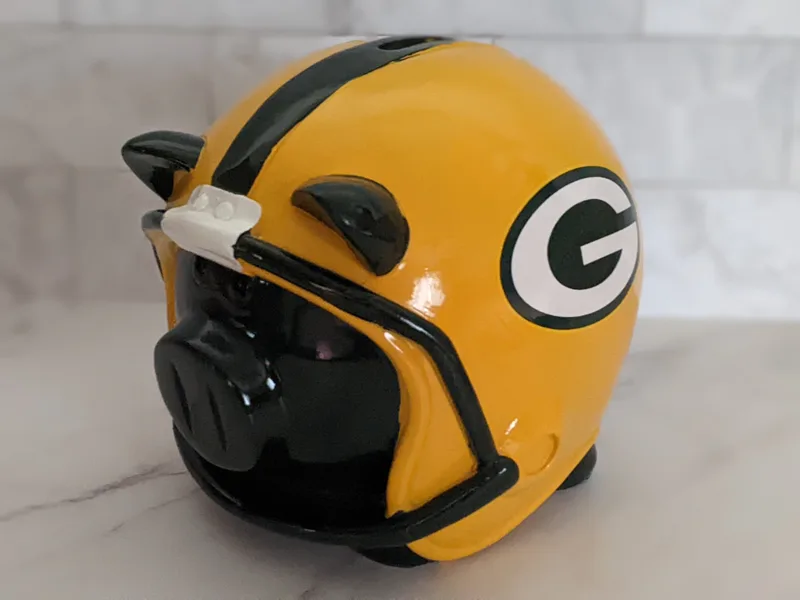 A green piggy bank that features a yellow NFL Green Bay Packers helmet with the Packer's logo.