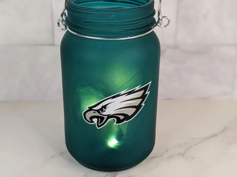 A frosted green canning-style jar with an NFL Philadelphia Eagles logo, that comes with a strand of mini white lights inside.