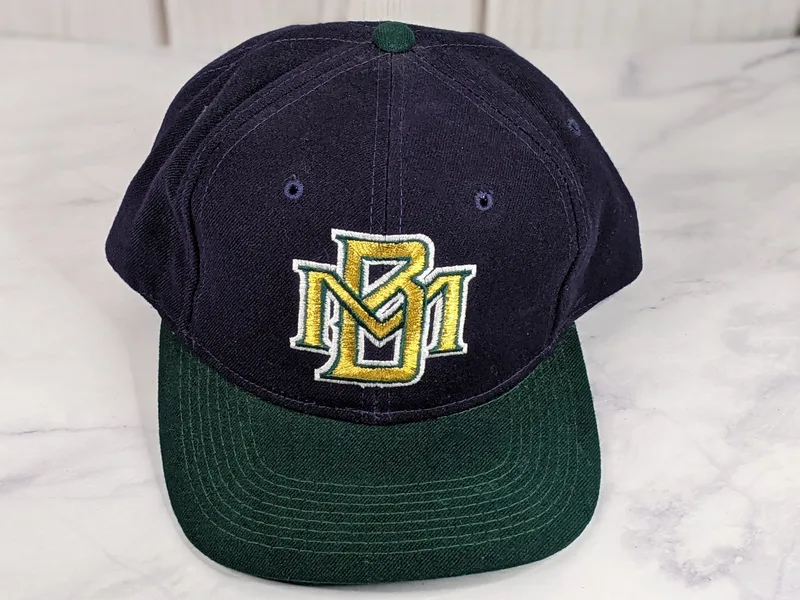 A navy blue baseball cap with a green bill and a vintage gold embroidered MB logo of the Milwaukee Brewers.