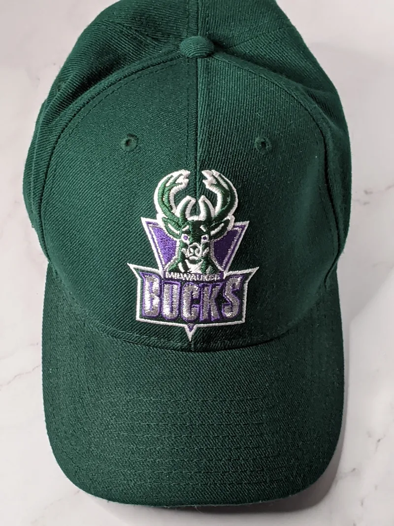 A green baseball cap with a purple deer vintage logo of the Milwaukee Bucks.