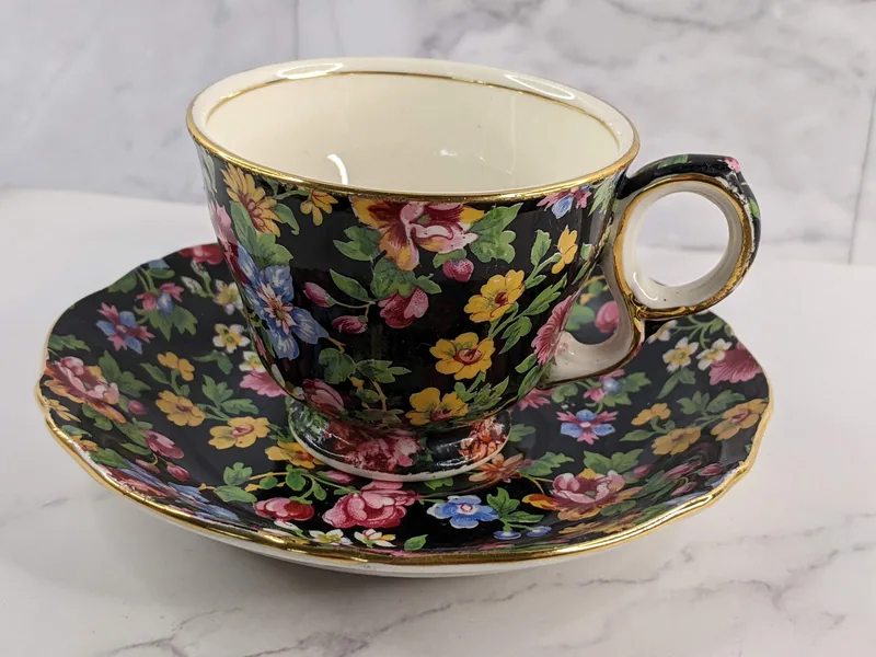 A teacup and saucer that is black on the outside with a pink and blue flower pattern.