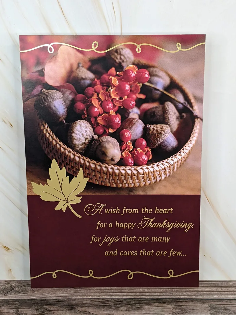 A Thanksgiving card with an image of nuts and berries in a basket with a golden leaf motif.