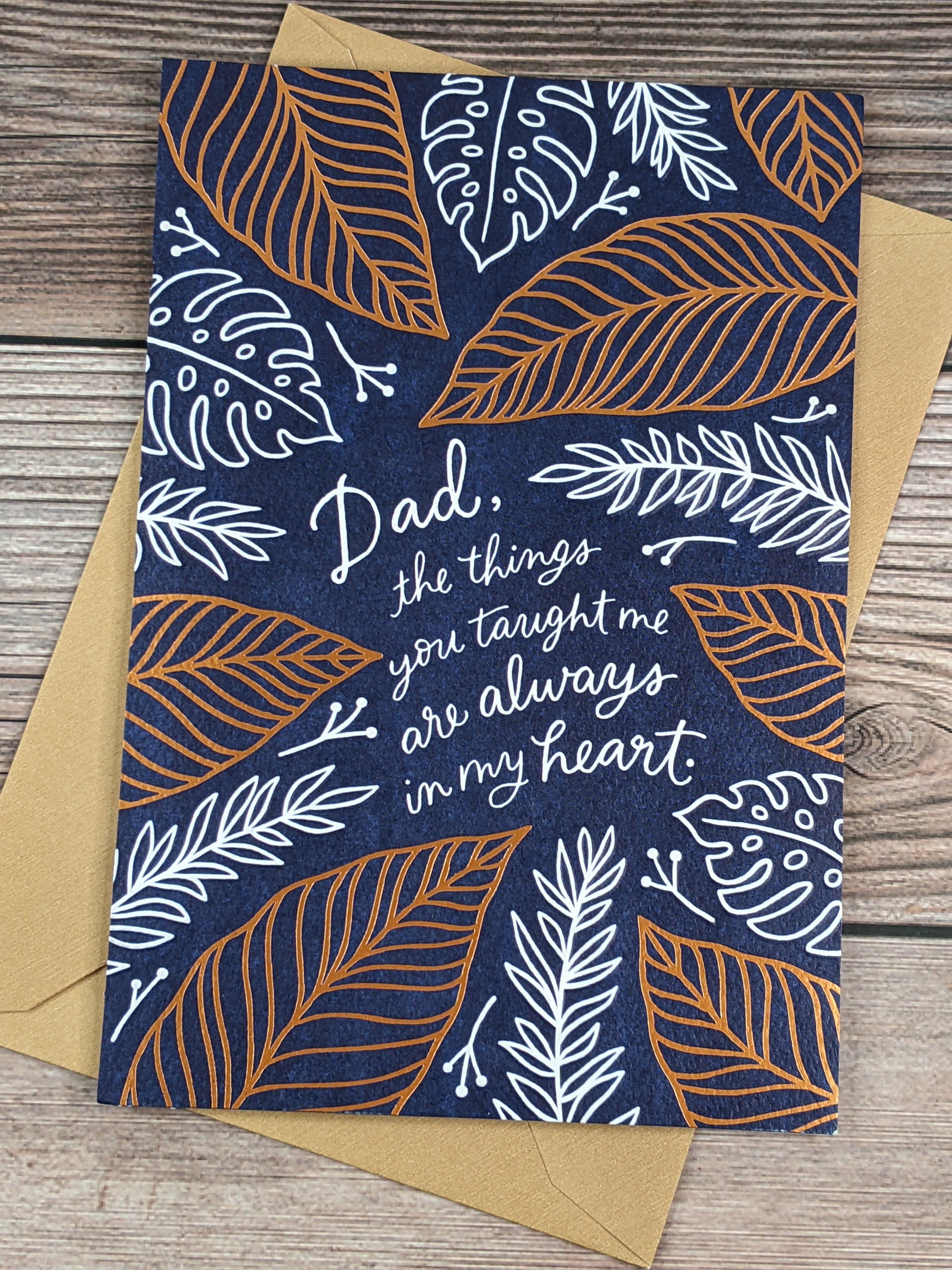 A Father's Day greeting card from a daughter, with a navy-blue cover featuring images of white and copper leaves.