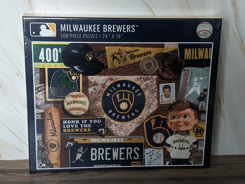 An MLB 500 piece puzzle in a box with images of Milwaukee Brewers memorabilia.
