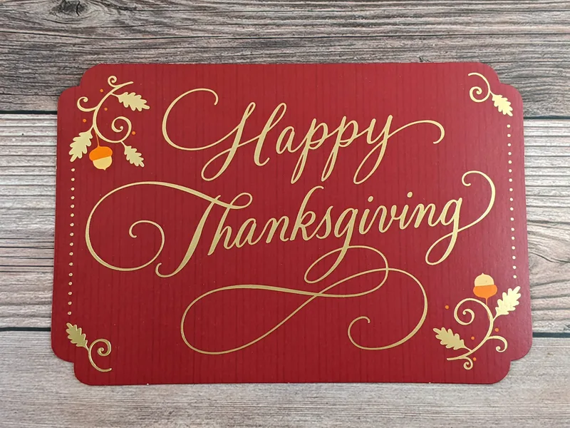 A red greeting card with the words "Happy Thanksgiving" in a fancy gold font.