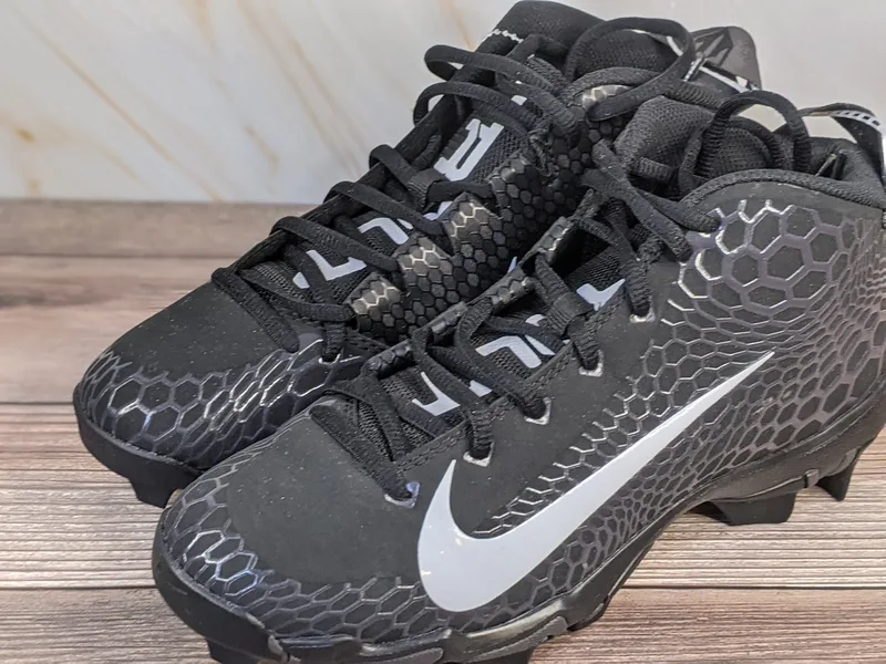 A pair of black cleats for youth by Nike Trout Fastflex, with a white swoosh and black laces.