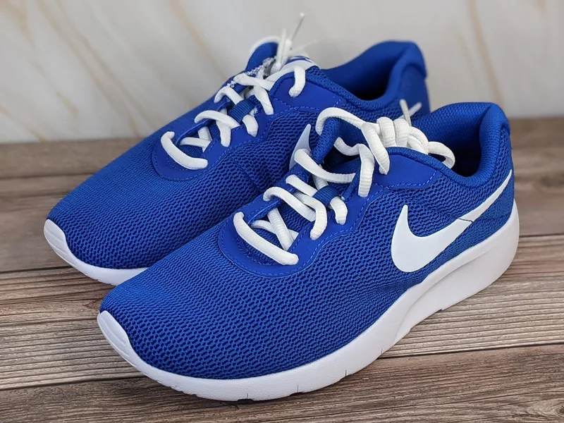 A pair of youth sized blue Nike running shoes with a white swoosh and laces.