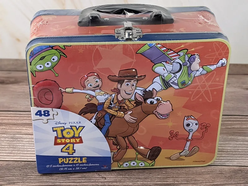 A red metal lunch box with images of Disney Pixar Toy Story characters on the front and a Toy Story puzzle inside.