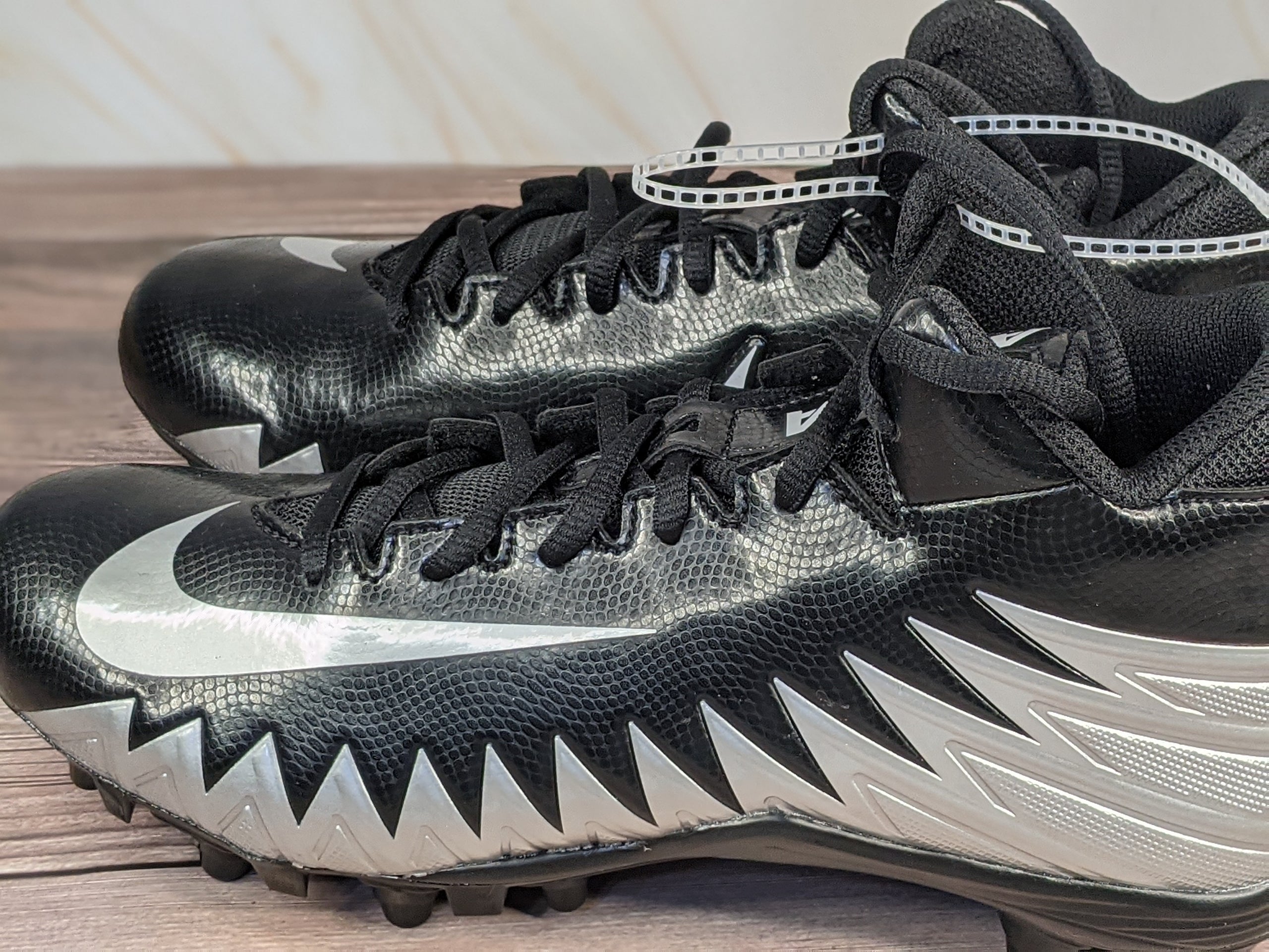 Nike Youth football cleats that are black with silver shark-patterned accents.