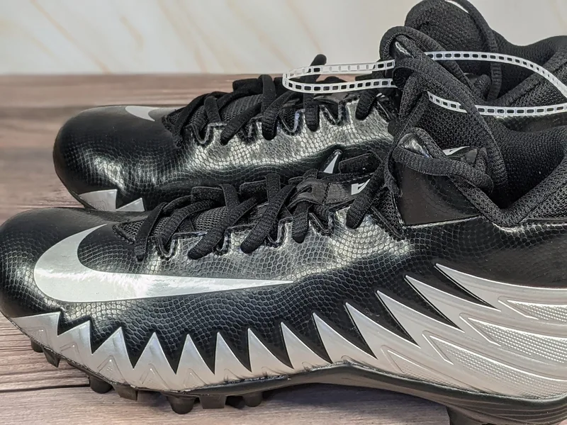 Nike Youth football cleats that are black with silver shark-patterned accents.