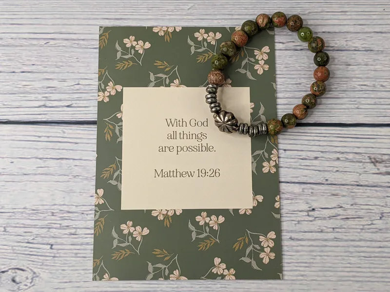 A Bible verse card with a beaded bracelet that has stone and metal beads. Matthew 19:26