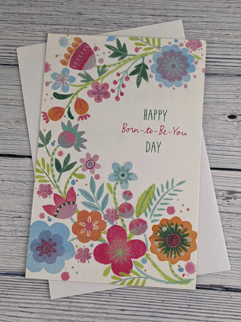 A birthday card with images of glittery pink, orange, and blue flowers on a white background.
