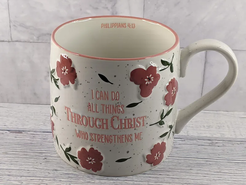 A large off-white ceramic mug with a design of pink flowers and a Bible verse, Philippians 4:13.