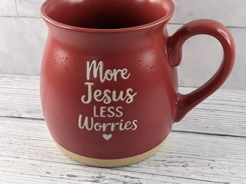 A red mug with the words "More Jesus Less Worries" displayed in white lettering with a heart symbol.