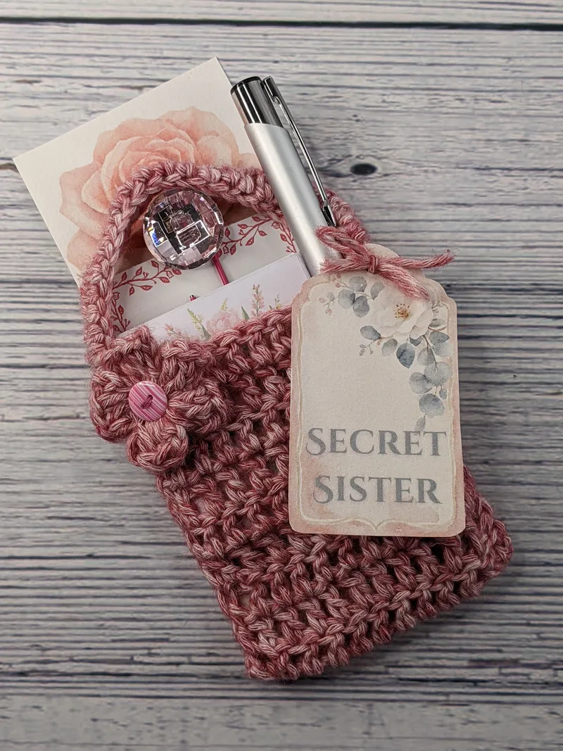 A crocheted pink gift bag with a Secret Sister gift tag and stationery items inside.
